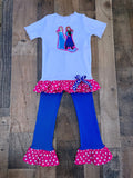 A children's two-piece outfit laid flat on a rustic wood plank background. The set includes a light blue short-sleeve top with a colorful Frozen graphic on the chest and a pink polka-dot ruffle hem, paired with bright blue flared leggings that have matching pink polka-dot ruffle hems and a blue-and-white polka-dot bow at the waist.