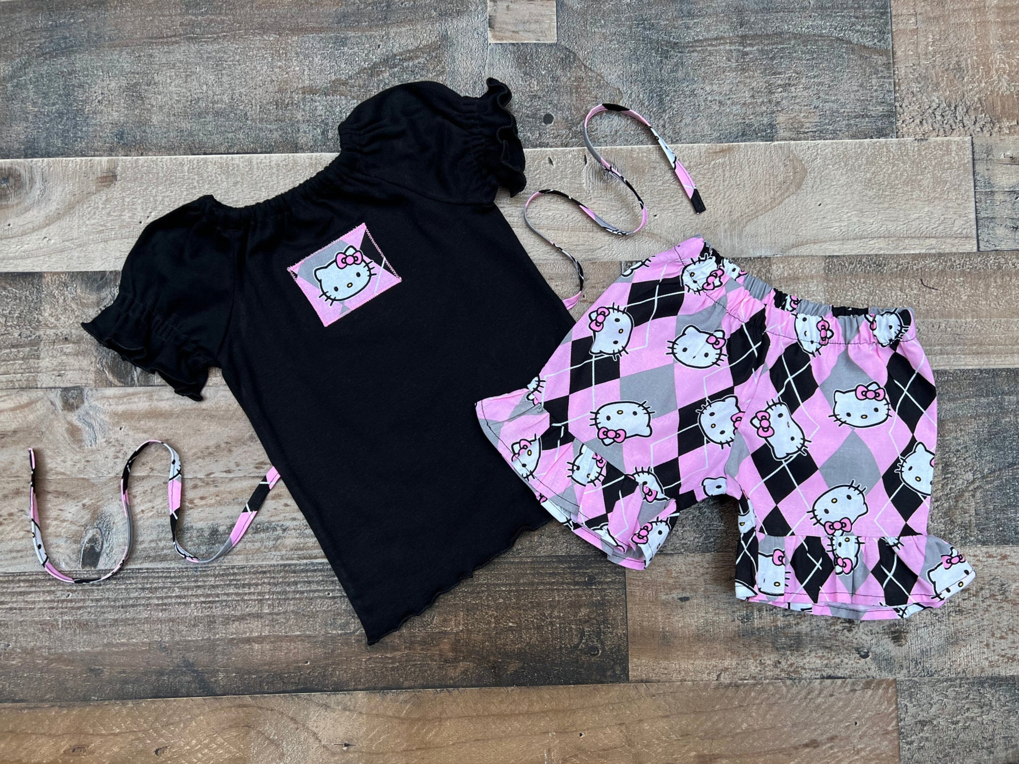 This cute Hello Kitty outfit would be perfect for a Hello Kitty theme birthday party celebration or just a fun day out in the sun. Top is a black comfy knit peasant style with ties that tie in back to keep fitted and a cute Hello Kitty applique on the front. The shorts are a cute Hello kitty pink gray and black fabric print.