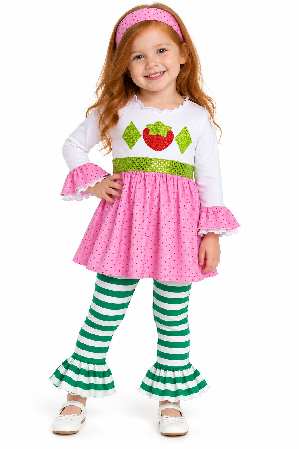 A young girl modeling a strawberry-themed costume dress with a white long-sleeve top, pink polka-dot skirt, green sequin waistband, green-and-white striped tights, and a pink headband on a white background.